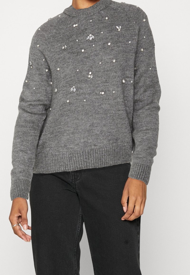 Grauer Strickpullover mit geripptem Saum und Bündchen, verziert mit verstreuten künstlichen Perlen und geminähnlichen Akzenten im gesamten Stoff.
