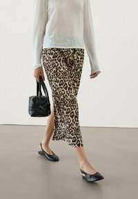 Maxi-Rock mit Leopardenmuster und seitlichem Schlitz, kombiniert mit einem transparenten weißen Langarmshirt und schwarzen flachen Schuhen, dazu eine kleine schwarze Tasche.
