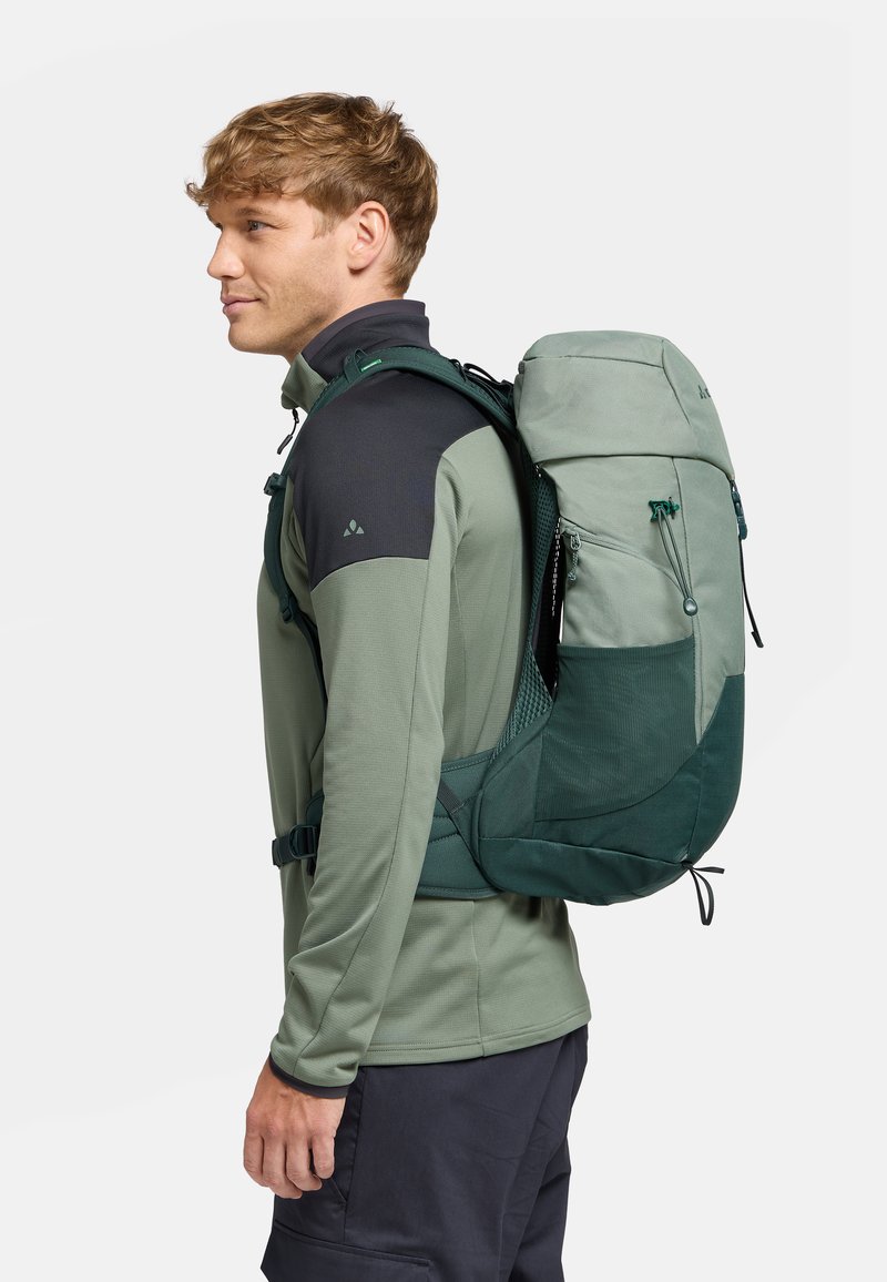 Sac à dos vert avec des bretelles réglables, un dos en mesh et plusieurs poches zippées. Le matériau semble durable, avec un design solide et une finition lisse.