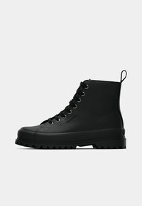 Botă neagră, cu șireturi, tip high-top, cu talpă groasă și rezistentă, dotată cu un mâner în spate, logo în relief pe lateral, aproape de șireturi.