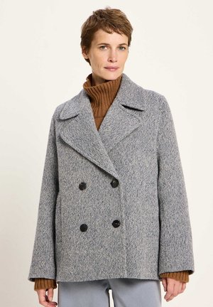 Gray double-breasted coat with large black buttons, made of textured fabric, featuring a collar and oversized fit. Brown turtleneck underneath.