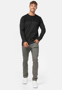 Sort og grå langærmet trøje med crew neck og struktureret overdel, parret med lysegrå lige bukser og hvide sneakers.