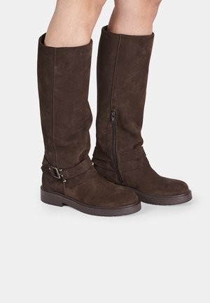 Barna velúr térd fölé érő csizmák cipzárral, széles nyílással és fémből készült csat részlettel rendelkező pánttal. Kényelmes lapos talp.