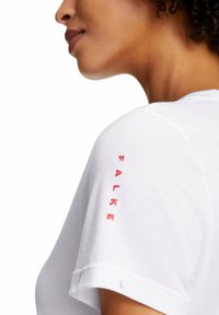 Weißes T-Shirt mit kurzen Ärmeln, das eine glatte Textur aufweist, mit dem roten 'FALKE'-Logo, das auf dem linken Ärmel gedruckt ist. Größenschild 'L' sichtbar.