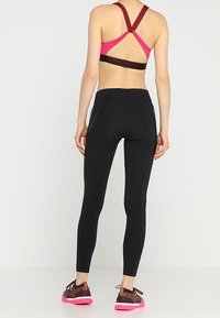 Leggings neri dal design aderente, abbinati a un reggiseno sportivo rosa e bordeaux con spalline incrociate e tessuto traspirante.
