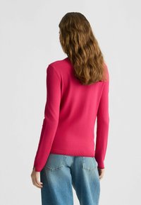 Taillierter Pullover in leuchtendem Pink, aus weichem Strickmaterial gefertigt. Verfügt über lange Ärmel und einen Rundhalsausschnitt, mit gerippten Bündchen und Saum.