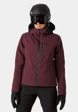 Veste de ski rouge avec une fermeture éclair à l'avant, un col haut et des accents noirs. Comprend une capuche douce en fourrure et un matériau imperméable. Les accessoires comprennent un casque noir et des gants.
