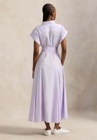 Μακρύ φόρεμα σε ανοιχτό μοβ με ρίγες, κοντά μανίκια, ζώνη στη μέση, πλαϊνές τσέπες και αέρινη φούστα. Συνδυασμένο με λευκά αθλητικά παπούτσια.