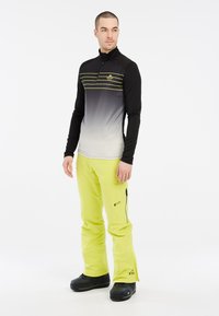 Zwarte en grijze gradient lange mouwen top met gele strepen, gecombineerd met felgele broek en zwarte sneeuwlaarzen; broek met ritsen.