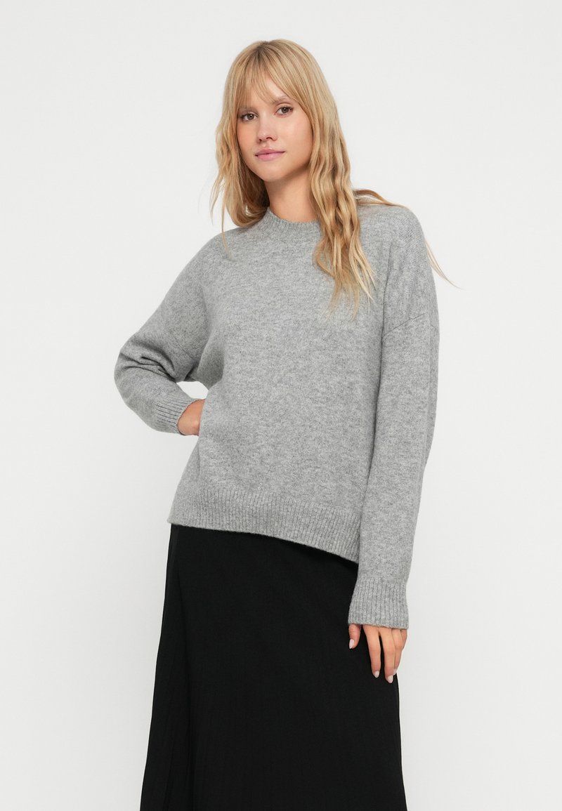 Szary sweter wykonany z miękkiej dzianiny, z okrągłym dekoltem, ściągaczami u rękawów i na dole oraz luźnym krojem i lekko opadającymi ramionami.