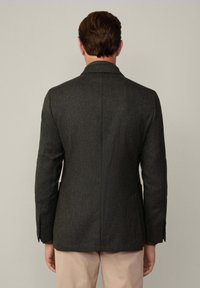 Blazer scuro e texturizzato con una fessura singola sul retro, rever a punta e vestibilità su misura. Presenta due bottoni e tasche laterali.