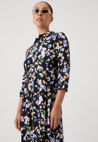 Mustriga lilleline kleit mustas värvis, millel on värvikad mustrid sinise, rohelise ja oranži toonides. Varustatud krae ja kolmeveerandi varrukatega. Kerge kangas.