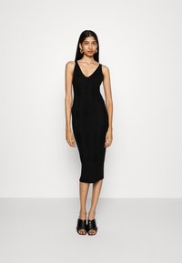 Black knitted midi dress with a V-neckline and ribbed texture. Features a fitted silhouette and intricate diamond patterns, paired with black open-toe mules.