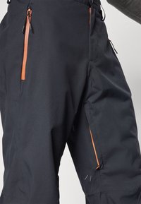 Black waterproof pants with zippered pockets featuring orange accents. Material appears durable and textured, designed for outdoor wear.