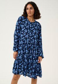 Robe bleu marine à manches longues avec un motif floral bleu clair, volant superposé et devant boutonné. Tissu doux avec une coupe décontractée.