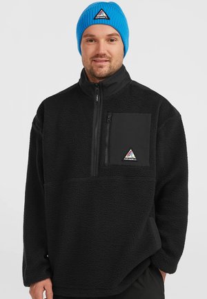 Black fleece pullover with a zippered pocket and textured fabric. Features a black panel on the chest and a triangular logo. Bright blue knit beanie.