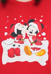 Mickey and Minnie Mouse dressed in Santa outfits, with Minnie kissing Mickey's cheek against a red background with white snowflakes.
