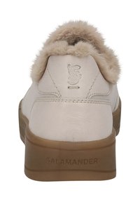 Weiße Lederschuhe mit einer sandfarbenen Gummisohle, strukturiertem Rückendetail und einem weichen Fellbesatz an der Ferse. Markenlogo ist in die Ferse eingeprägt.