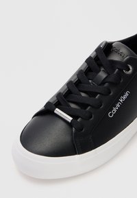 Fekete bőr sportcipő kerek orral, fehér gumitalppal, fekete fűzővel és ezüst részletekkel az oldalon. Calvin Klein logóval rendelkezik.
