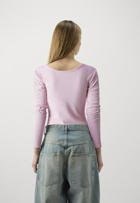 Maglietta a maniche lunghe a coste rosa chiaro con ampia scollatura rotonda, abbinata a jeans in denim azzurro chiaro a taglio morbido con due tasche posteriori.