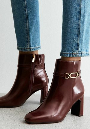 Bottes chelsea bourgogne en cuir brillant, avec des orteils pointus, des accents en métal doré, et une fermeture éclair sur le côté. Les talons bloc offrent une stabilité.