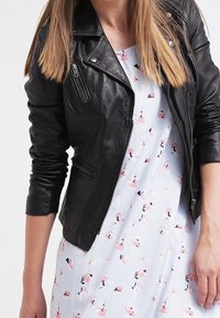 Schwarze Lederbikerjacke mit Reißverschlusstaschen, getragen über einem hellblauen Kleid mit einem Blumenmuster in Pink und Schwarz.