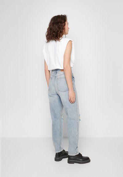 Top branco leve sem mangas com acabamento texturizado, combinado com jeans de cintura alta azul claro com detalhes desgastados e sapatos pretos.