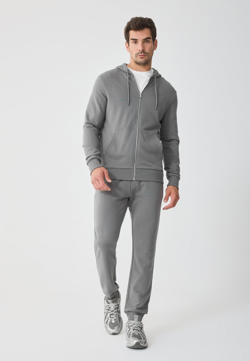 Grijze rits hoodie met verstelbare trekkoorden, gecombineerd met bijpassende joggers. Soepele katoenmix stof, relaxte pasvorm en ribgebreide manchetten.