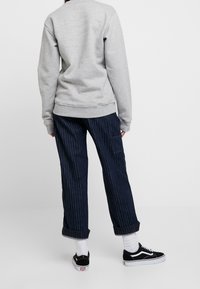 Sweat-shirt gris avec poignets et ourlet côtelés, associé à un pantalon bleu marine à fines rayures avec poche latérale et ourlets retroussés. Baskets noires avec semelles blanches.