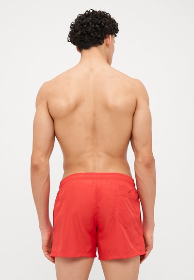 Shorts de bain rouges avec une taille élastique, longueur au-dessus du genou et une poche arrière. Texture lisse et design simple sans motifs.