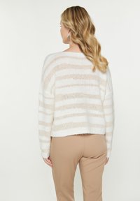 Gestreepte lichte trui in wit en beige, met een relaxed fit en een geribbelde zoom. De textuur lijkt zacht en gebreid.