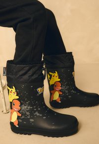 Zwarte rubberen laarzen met eengequilted rand hebben levendige Pokémon ontwerpen van Pikachu en Charmander, grijze spetterdetails en een gestructureerde zool.