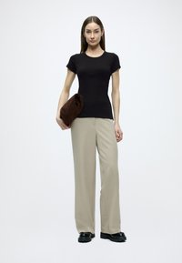 Μαύρο κοντομάνικο πουκάμισο σε συνδυασμό με ανοιχτό μπεζ παντελόνι με φαρδιά πόδια και σκούρο καφέ τσάντα χειρός, με ομαλή υφή και μίνιμαλ σχεδιασμό.