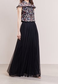 Black maxi skirt with a flowy silhouette, paired with a floral patterned top featuring a ruffled collar and sheer accents.