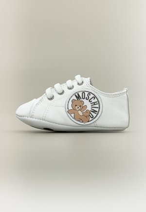 Scarpa da ginnastica bianca per bambini con lacci bianchi e una toppa rotonda sul lato con un orsetto e la scritta "MOSCHINO".