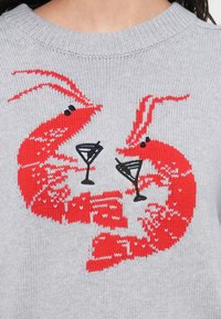 Pull en maille gris avec deux homards rouges tenant des verres à martini noirs, avec une broderie détaillée des motifs corporels et des antennes.