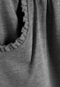 Gros plan sur un tissu gris doux avec un bord froncé le long d'une couture courbe, montrant la texture du tricot et de légers plis.