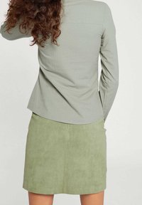 Vaaleanvihreä pitkähihaisen paidan pusero, jossa on kaareva helma; yhdistetty samansävyiseen vaaleanvihreään mokkahameeseen, jossa on sileä pinta ja istuva muotoilu.