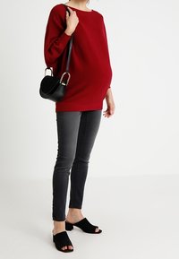 Punainen neulottu villapaita, löysä istuvuus, pyöreä kaula-aukko. Mustat skinny-farkut ja avonaiset mustat tolppapohjakengät. Pieni musta olkalaukku, jossa on kultaiset yksityiskohdat.