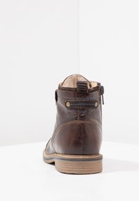 Hnědá kožená kotníková bota s béžovou podrážkou, modrým prošíváním a vnitřním kožíškem, zobrazená zezadu na bílé ploše a pozadí.