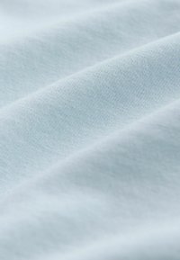 Világoskék szövet puha tapintással, egyszínű szövettel, redőkkel és sima felülettel, enyhe árnyalatváltozásokkal.