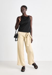 Czarny top bez rękawów o strukturalnym designie, w połączeniu z jasnobeżowymi spodniami wide-leg z wiązanym detalem w pasie. Odpowiednie obuwie to masywne czarne sandały.