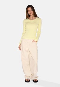 Gul ribbad långärmad tröja i kombination med löst sittande beiga byxor. Skorna är svarta platta sandaler. Enklare och avslappnad outfit.