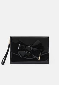 Pochette en cuir verni noir avec un grand nœud sur le devant et un logo doré. Comprend une fermeture éclair et une poignée pour le poignet.