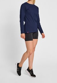 Marinblå långärmad skjorta, i kombination med svarta träningsshorts. Skorna har en svart och vit design med texturerad ovandel och dämpad sula.