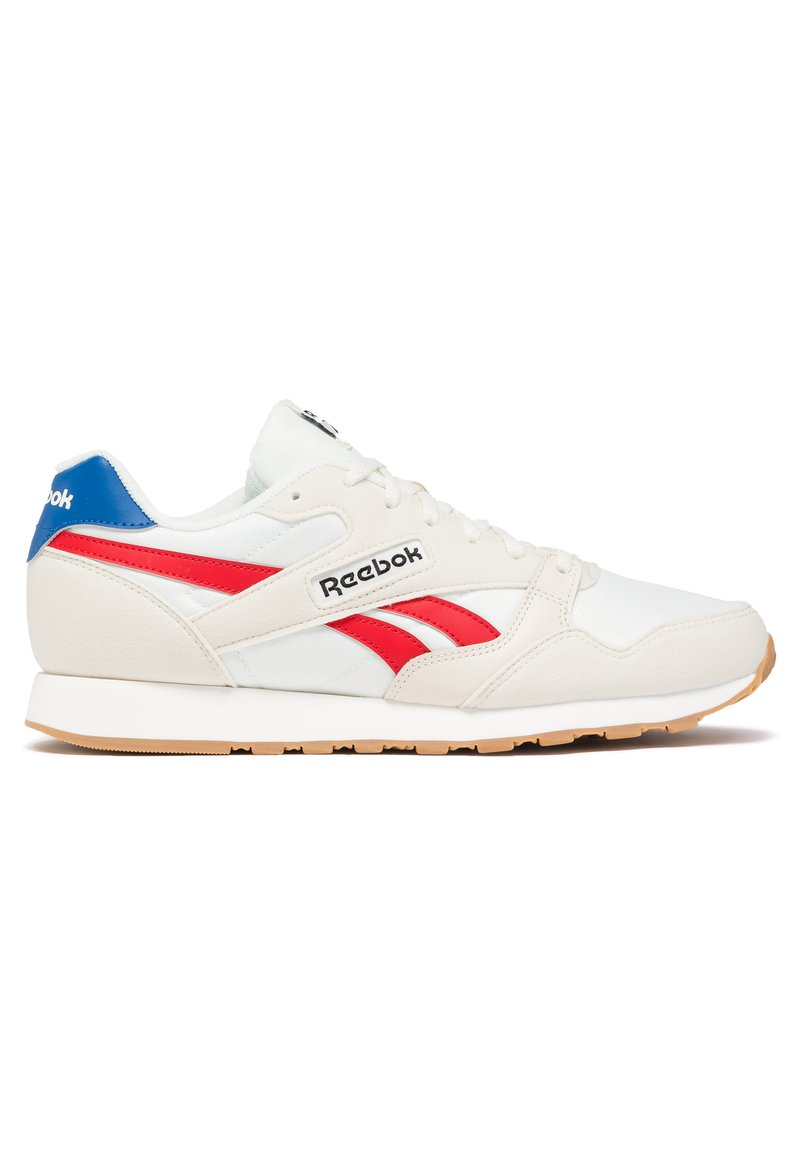Zapato deportivo blanco con acentos rojos y azules, que presenta un diseño en capas, materiales texturizados y una suela de goma con acabado de goma.