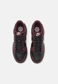 Paire de baskets Nike noires et rouge foncé avec logos Swoosh blancs, lacets noirs et motif floral sur les semelles intérieures, vue de dessus.