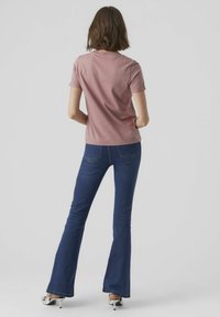 Tegelijkertijd aansluitend roze T-shirt met korte mouwen en een gladde stof. Gecombineerd met donkere spijkerflared jeans, subtiele stiksels en glanzende zilveren hakken.