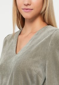 Lysegrønn v-hals topp med en rilletekstur, laget av mykt stoff og med en litt avslappet passform, som fremhever et rent og enkelt design.