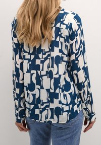 Langärmlige Bluse in Blau- und Weißtönen mit entspanntem Schnitt, ausgestattet mit abstrakten Formen, Knopfmanschetten und abgerundetem Saum.